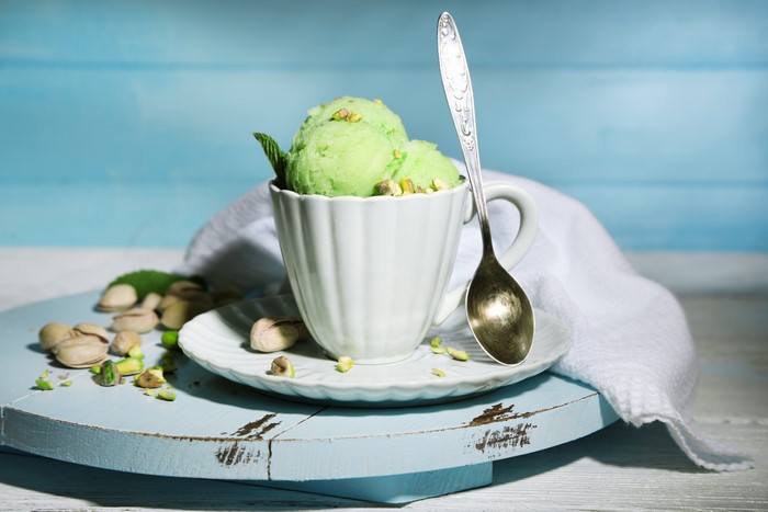 Pistachio ice cream in a cup with pistachios and a spoon