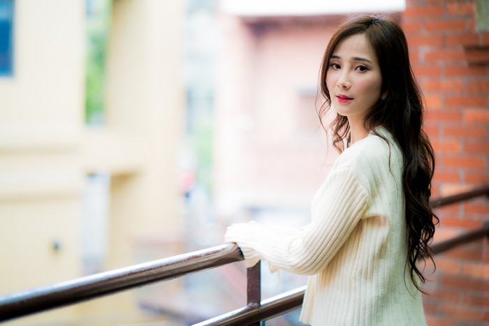Asian woman with brown hair in a sweater on a balcony