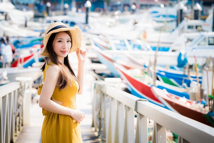 Asian woman in yellow dress and hat at a harbor