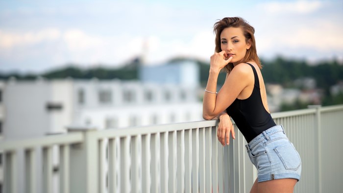 Woman in black swimsuit and denim shorts leaning on fence