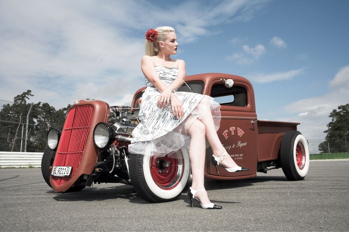 Blonde girl in retro dress sitting on a hot rod truck