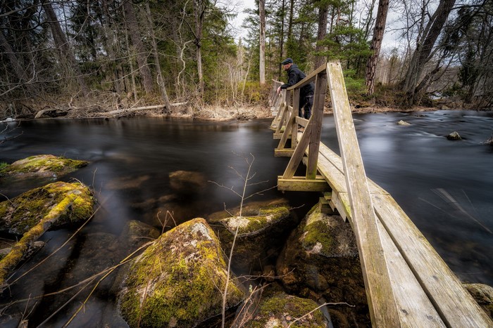 Man on a wooden bridge over a river with stones