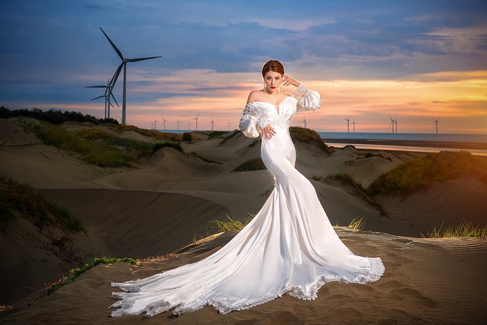 Asian woman in wedding dress posing near wind turbines