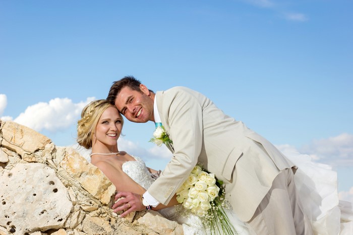 Bride and Groom posing on rocks with blue sky