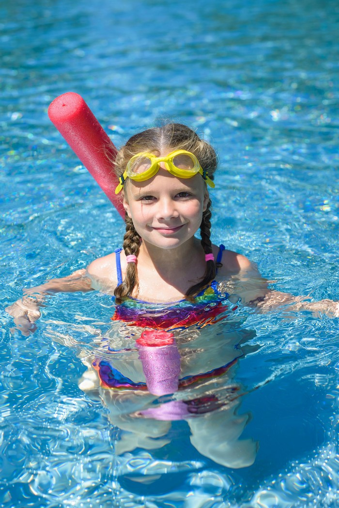 Girl in a swimming pool with goggles and pool noodle