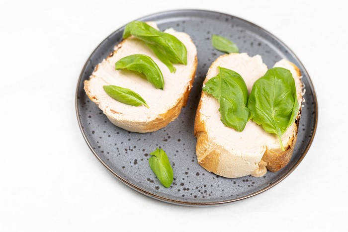 Two slices of bread with spread and basil leaves on a plate