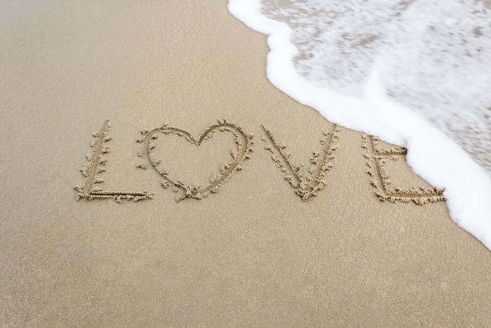Love written in sand with a heart and wave