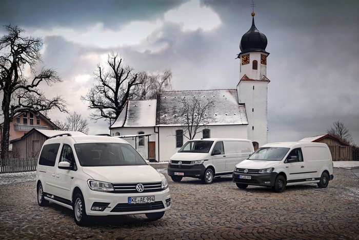 Three white Volkswagen vans and Caddy in front of a church