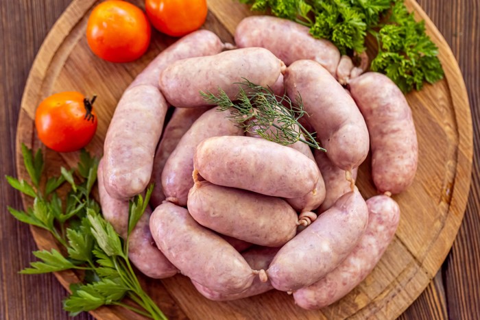 Raw sausages with tomatoes and parsley on a cutting board
