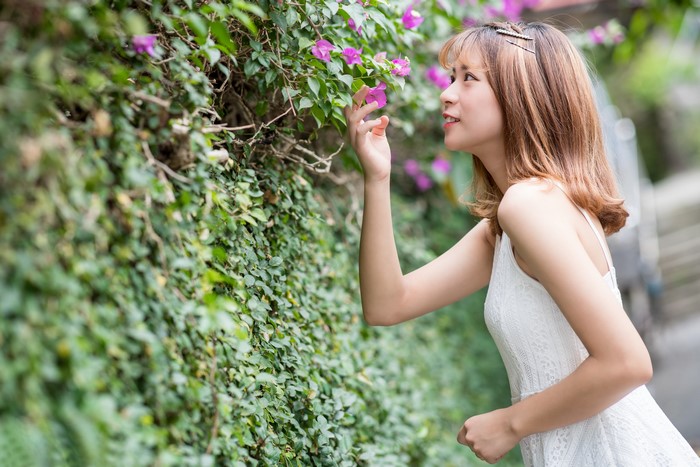 Asian woman smelling flowers on a vine-covered wall