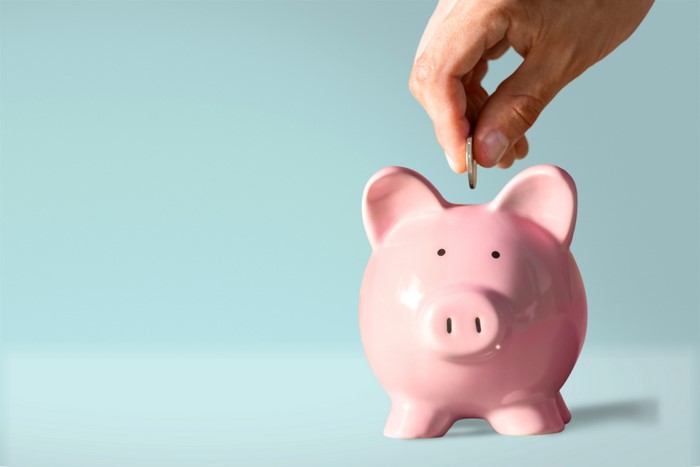 Hand putting coin in pink piggy bank