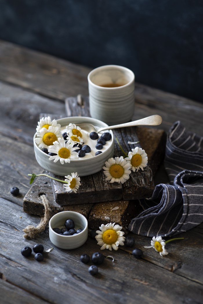 Yogurt with blueberries and chamomile flowers on wooden planks