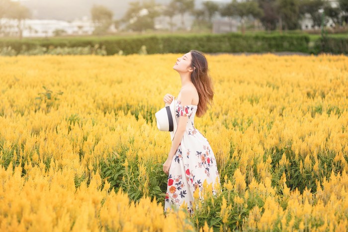 Woman in a floral dress in a yellow field holding a hat