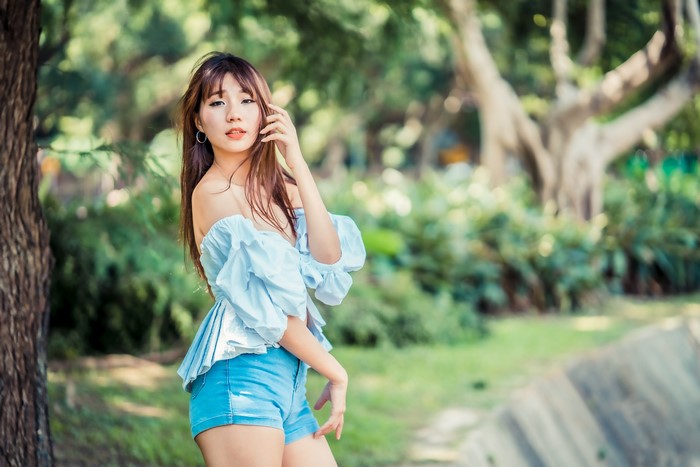Asian woman in off-shoulder blouse and shorts posing in park