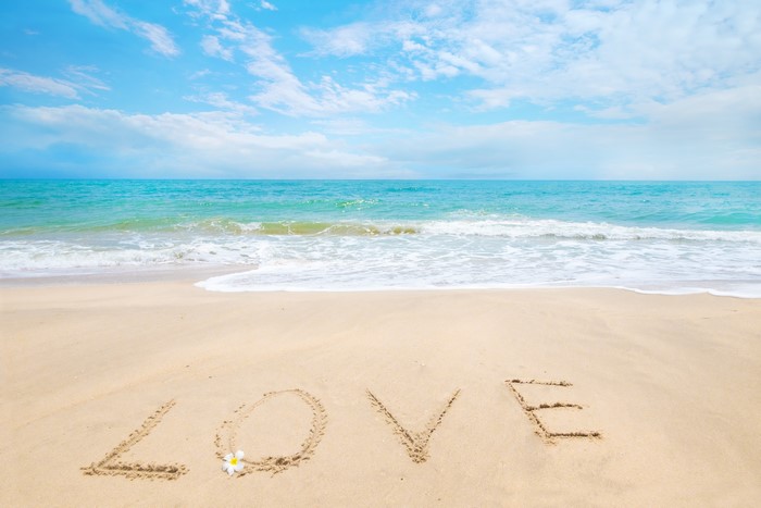 Love written in sand on a beach with the sea and sky