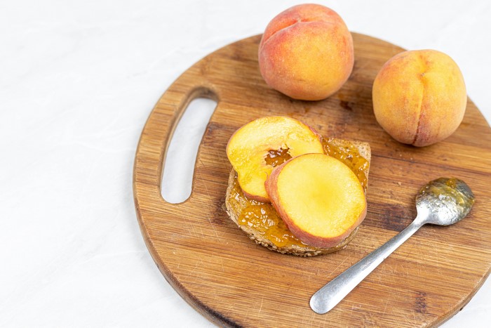 Peaches and jam on toast with spoon on cutting board