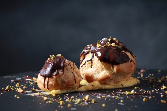 Two chocolate cream puffs with pistachios
