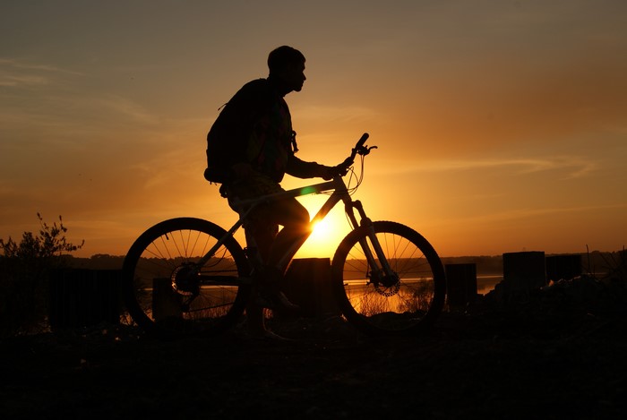 Man on bicycle silhouetted against sunset
