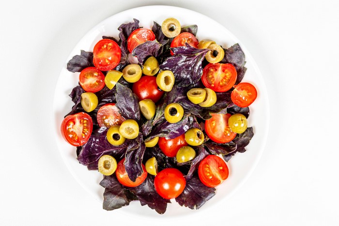 Salad with tomatoes, olives, and basil on a white plate