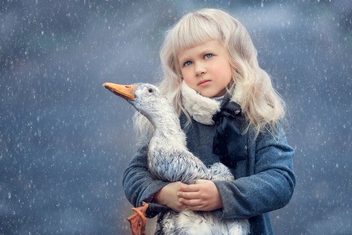 Blonde girl holding a goose in the snow