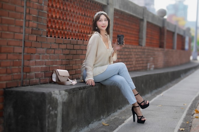 Woman in Jeans and Heels Sitting by Brick Wall