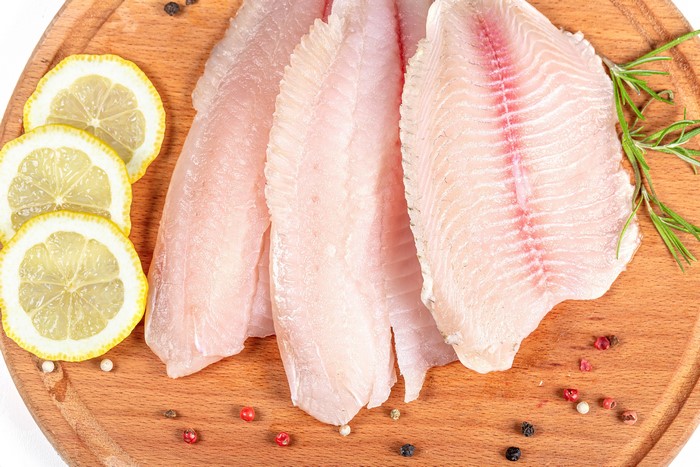 Raw Fish Fillets with Lemon Slices and Spices on Cutting Board