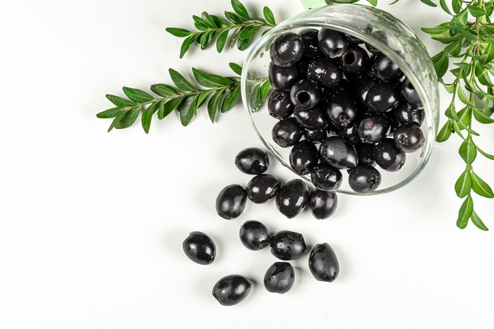Black olives spilling from a glass bowl with green branches
