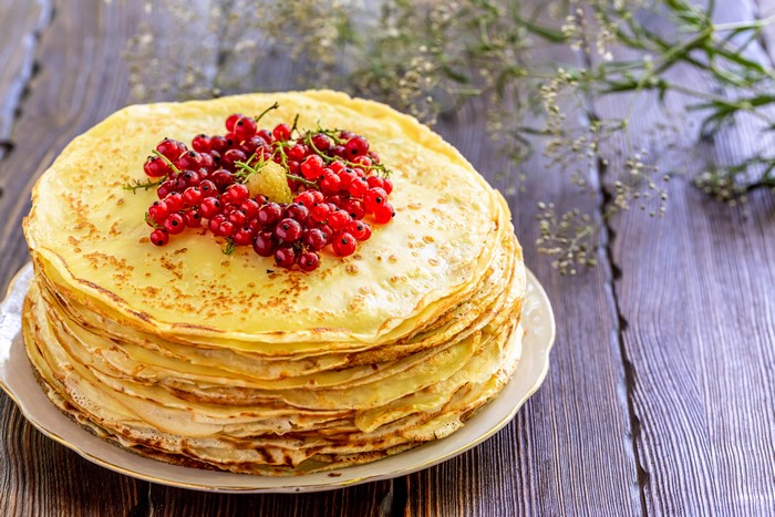 Stack of pancakes with red currants on a wooden table