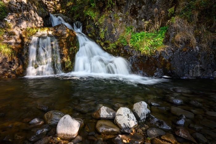 Waterfall cascading over rocks into a stream with stones