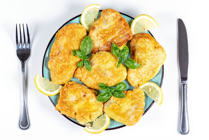Fried fish with lemon and basil on a plate with fork and knife
