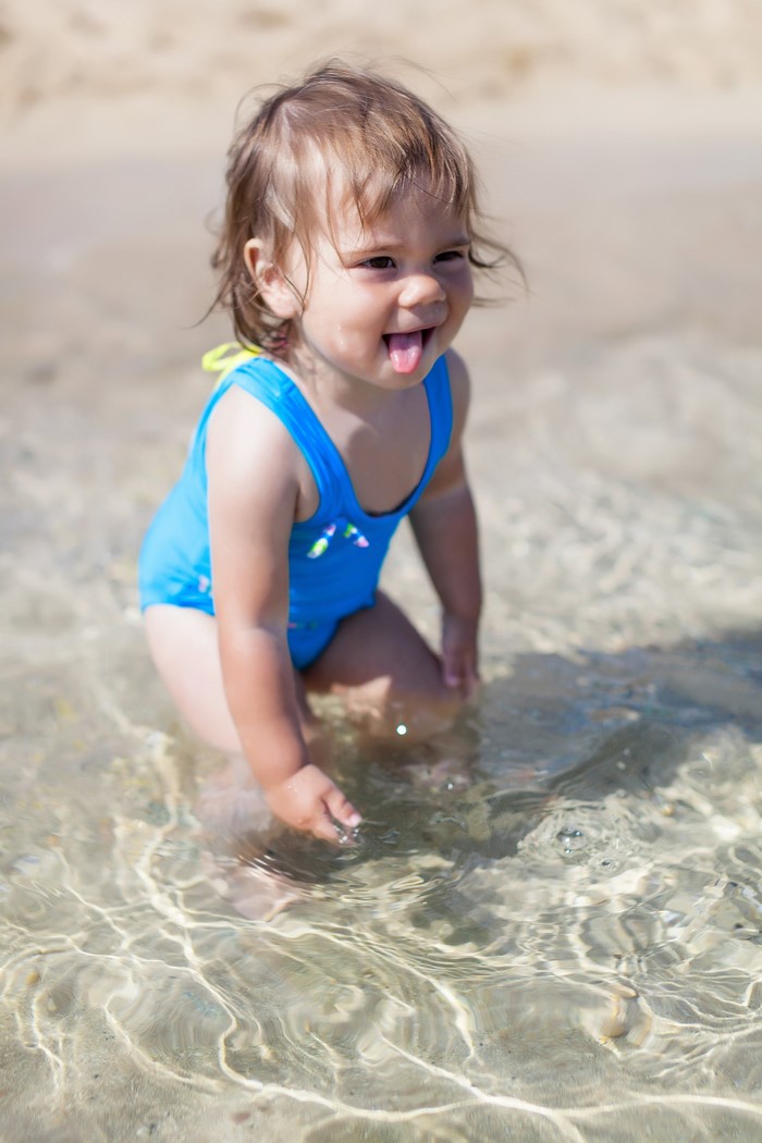 Baby girl in blue swimsuit playing in shallow water