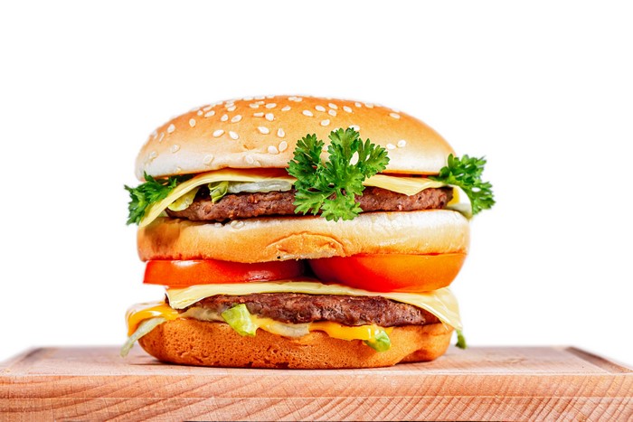 Double cheeseburger with lettuce, tomato, and parsley on a cutting board