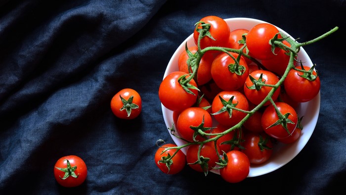 Tomatoes on a vine in a white bowl on a dark cloth