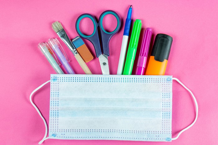 School supplies in a face mask on a pink background
