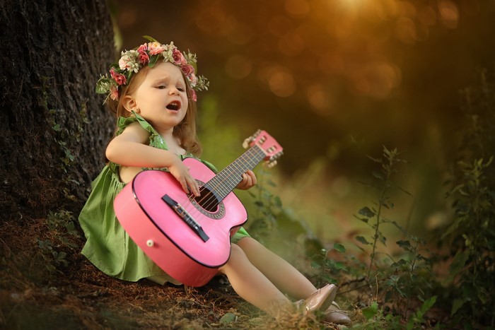 Little girl with flower wreath playing guitar