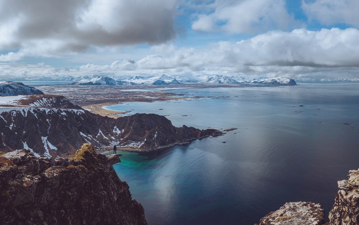 Man on cliff overlooking sea and snowy mountains in Norway