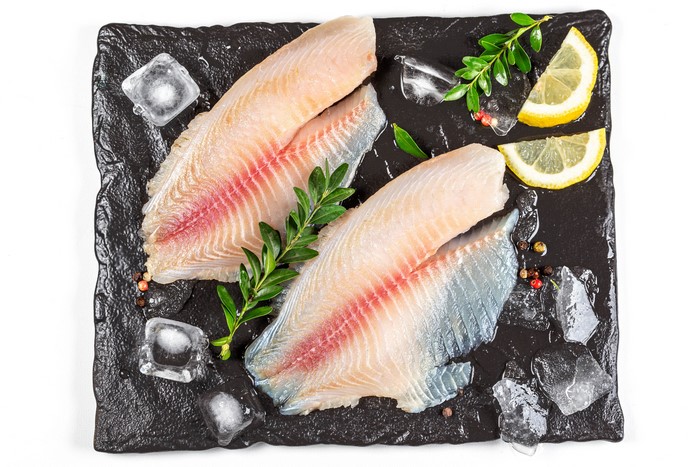Raw fish fillets with lemon and ice on a slate plate