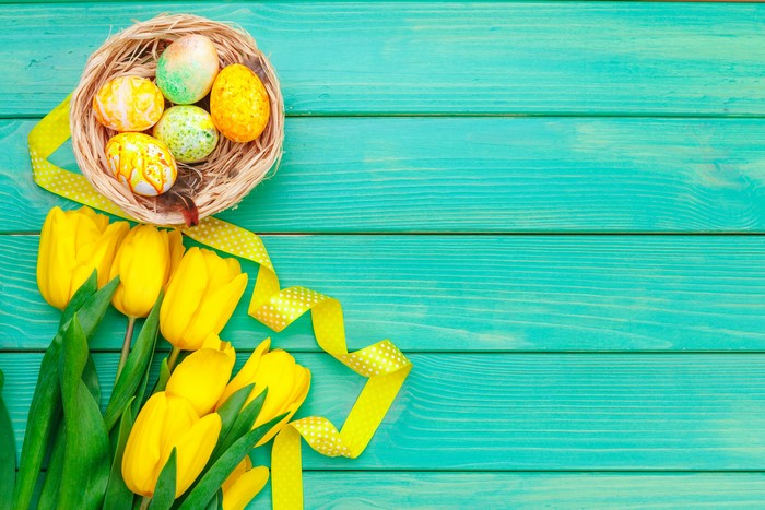 Easter eggs in a nest with yellow tulips and ribbon on wood planks