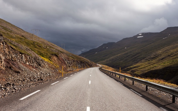 Empty road through a mountain valley under stormy clouds