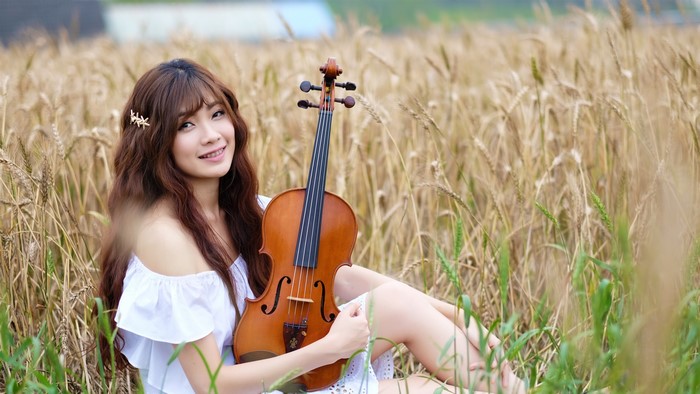 Asian woman with violin in wheat field