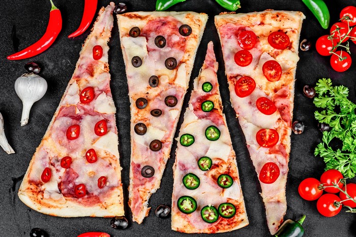 Pizza slices with chili peppers, olives, and tomatoes