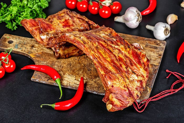 Smoked ribs with chili peppers, garlic, and tomatoes on a cutting board