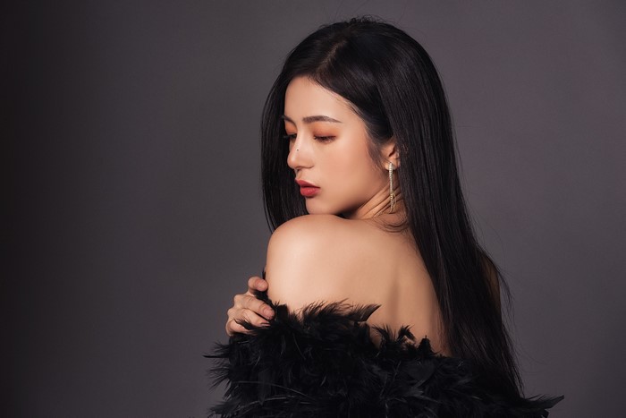 Brunette girl with black feathers on gray background