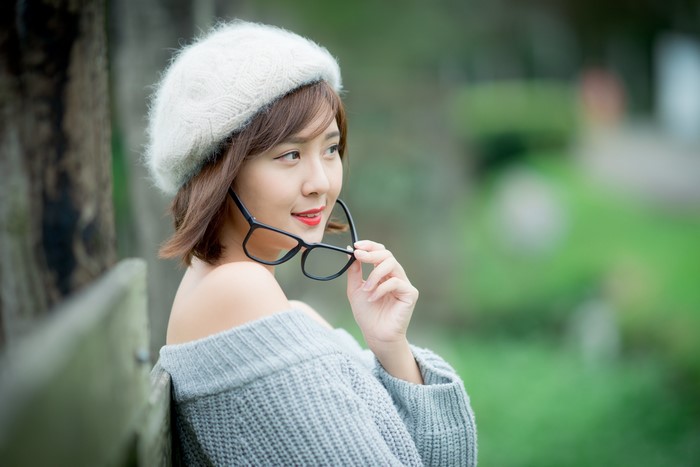 Asian woman wearing a beret and sweater holding glasses