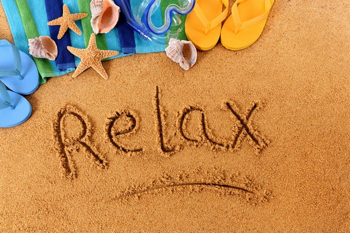 Relax written in sand with beach accessories
