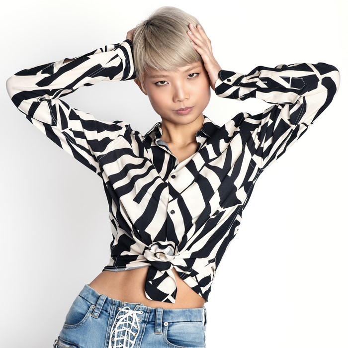 Asian woman with blonde hair in a patterned shirt and jeans