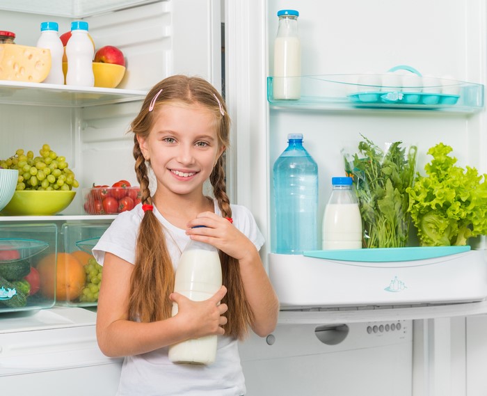 Girl holding milk bottle in front of refrigerator