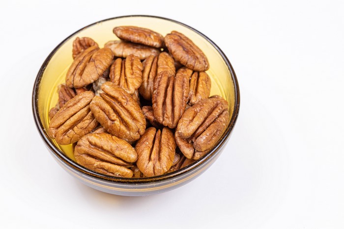 Pecans in a yellow bowl on a white background