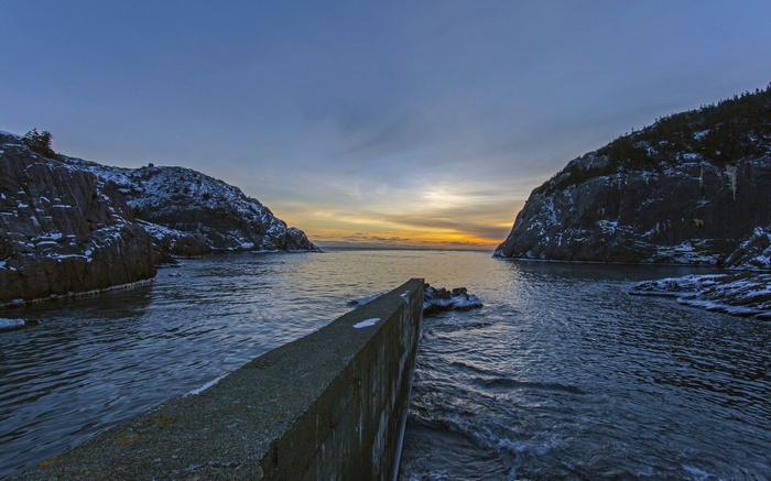 Concrete pier in a bay at sunrise with snow-covered hills