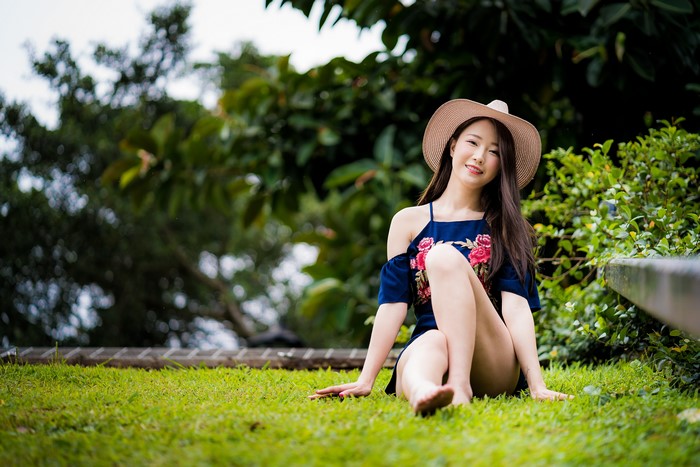 Asian woman sitting on grass wearing a hat